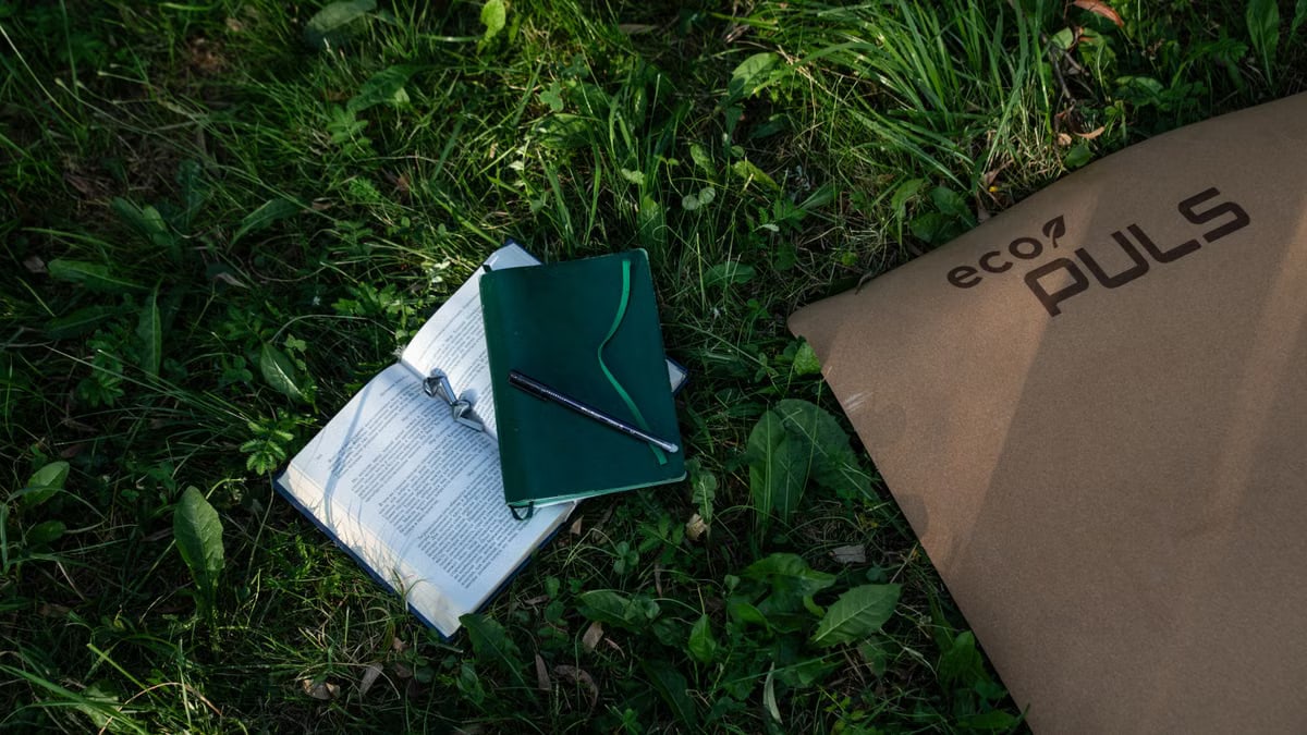 Open book, notebook, and eco packaging on grass, embodying outdoor study and sustainability.