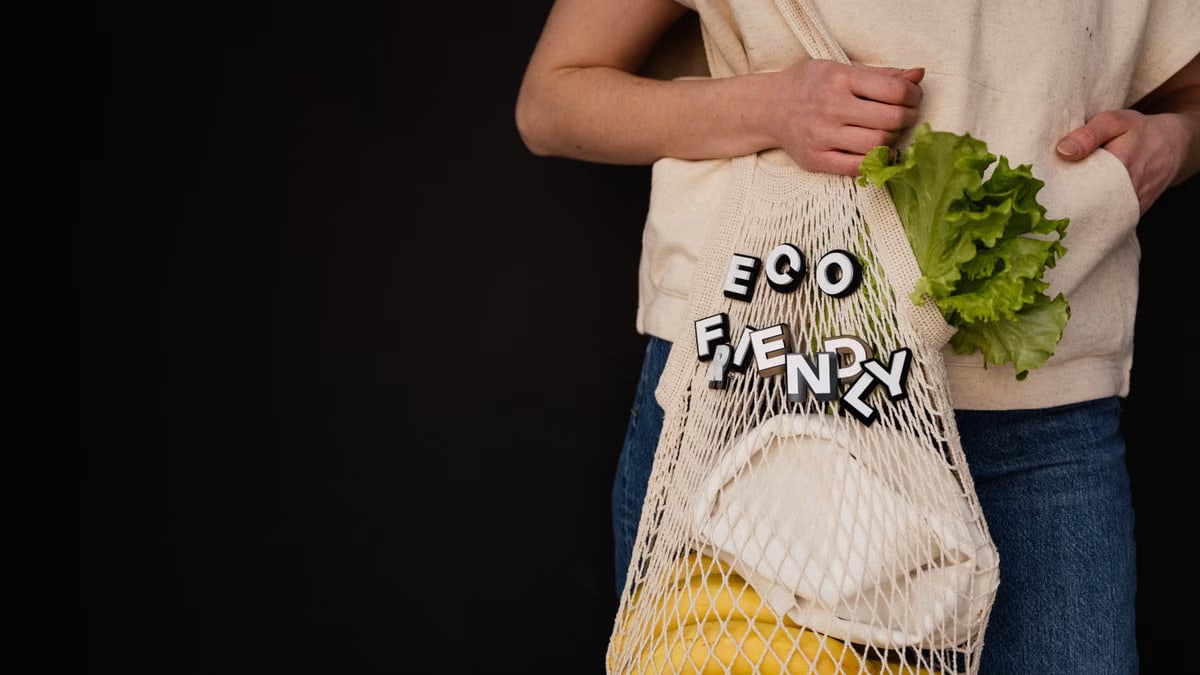Person holding a string bag with eco-friendly text, lettuce, and bananas against a dark background.